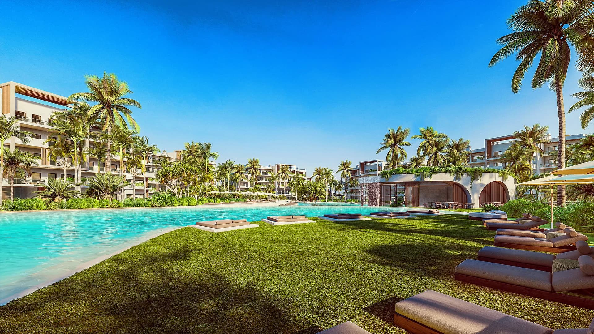 Beach-entry pool with sun loungers on the lawn and the buildings behind