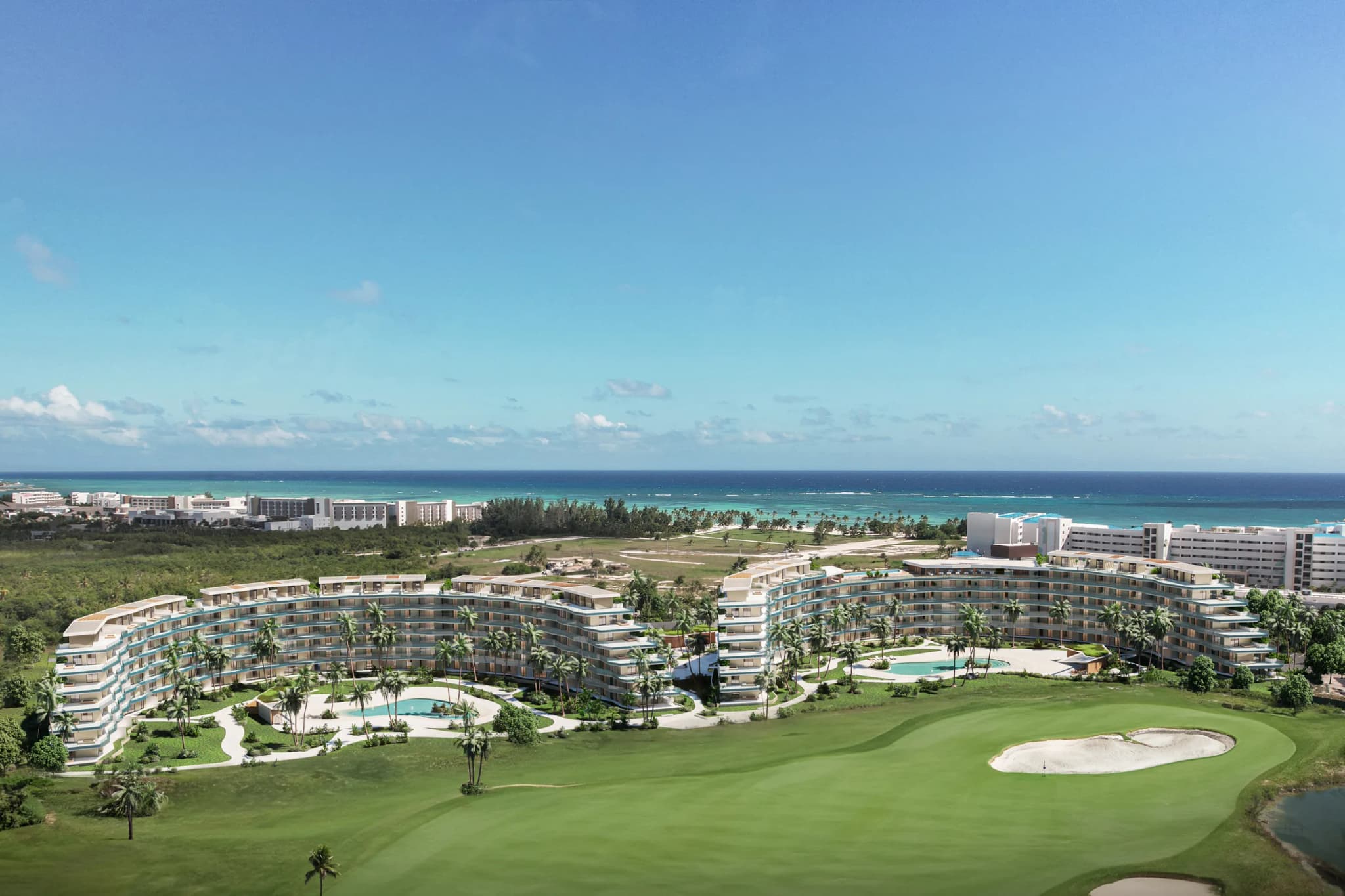 Vista aérea de Crystal Garden: los edificios curvos rodean las piscinas junto al campo de golf, con el mar detrás